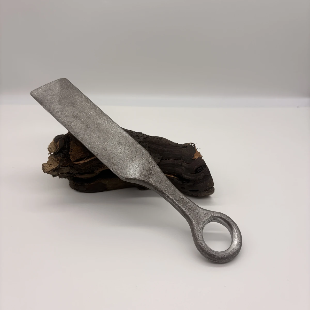 Batte de vannier en acier à anneau de redressage, posée sur un morceau de bois brut