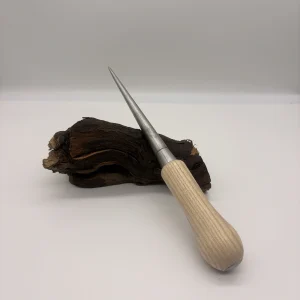 Épissoir de vannier conique en acier, manche en bois clair, posé sur un morceau de bois brut
